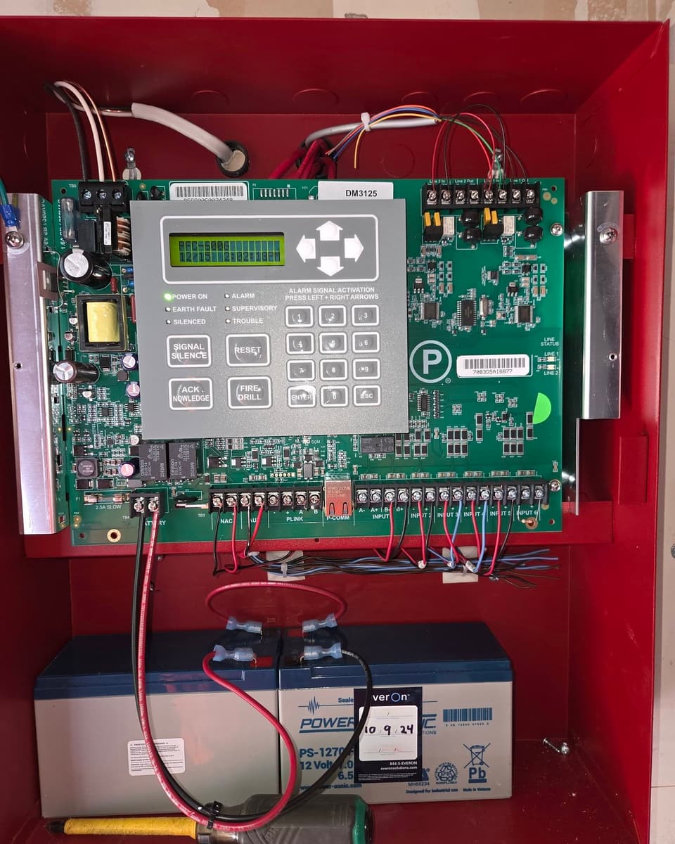 Open fire alarm control panel showing the main board, terminals and standby batteries